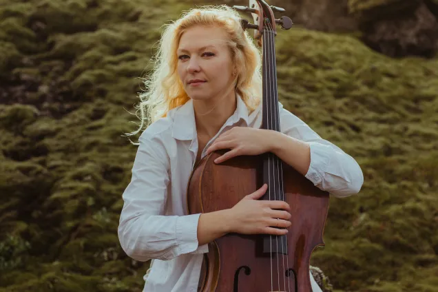 Amalie Stalheim with her cello in a mountain landscape. Photographer: Kristina Ratciz.