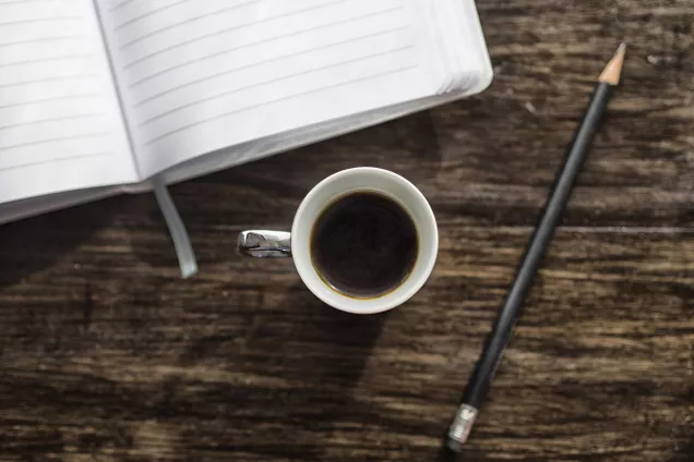 Kaffekopp, anteckningsbok och penna. Foto.