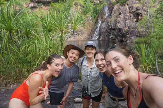 Fem utbytesstudenter står framför ett vattenfall och ler. Foto.