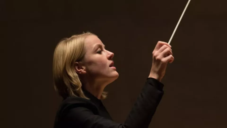 Bilden är ett porträtt på dirigenten Ruth Reinhardt när hon dirigerar. Bakgrunden är mörk.