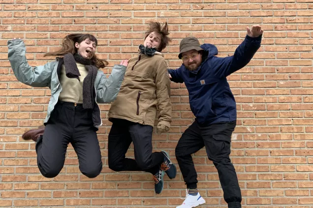Tre studenter hoppar i luften framför en tegelvägg. Foto.