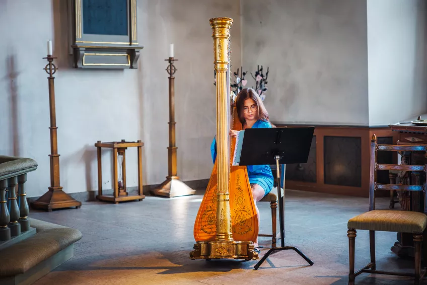 Malin Olsson spelar harpa i en kyrka. Foto. 