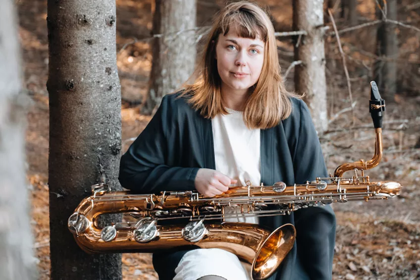 Alice Andersson i skogen med sin saxofon i famnen. Foto. 
